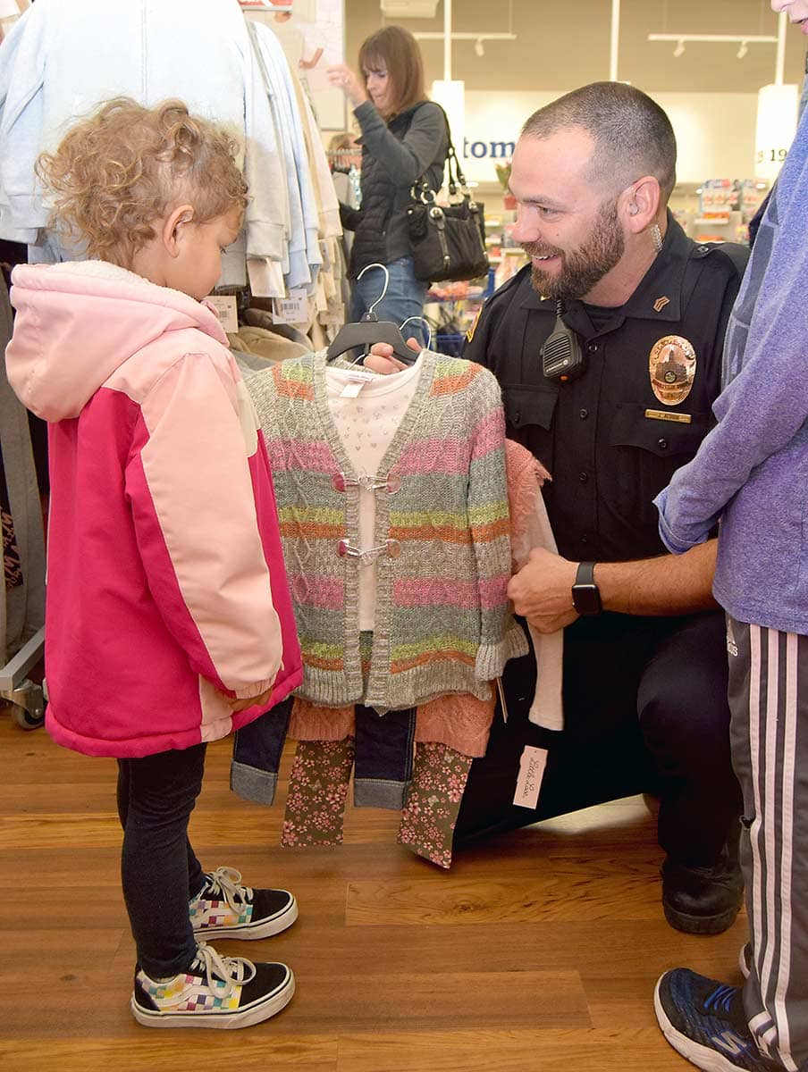 Officer helping little girl shop for clothes at "Shop with a Cop" charity event.
