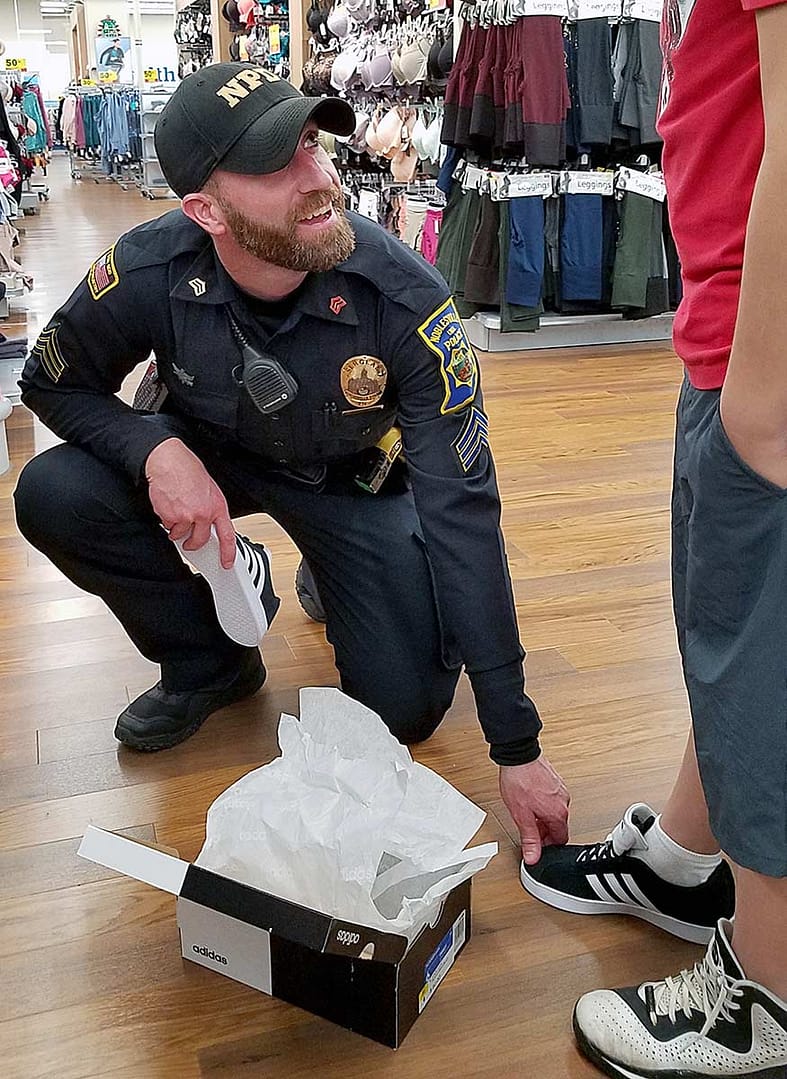 Officer helping little boy buy shoes at "Shop with a Cop" charity event.